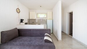 A compact living space with a sofa, kitchenette, and a door leading to another room.