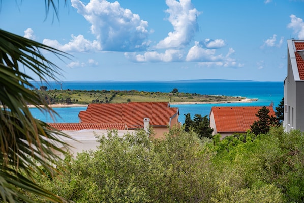 A coastal view with red-roofed buildings, a clear sky, and a distant shoreline.