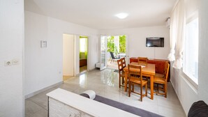 A spacious room with a dining area, a television, and a window with curtains.