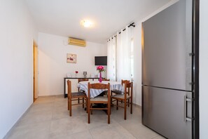 Ein Essbereich mit Tisch, Stühlen, einem Kühlschrank und einem Fernseher an der Wand.