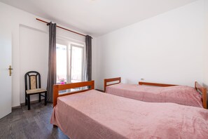 Une chambre avec deux lits, une chaise, une fenêtre avec des rideaux et une porte.