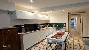 A compact kitchen with white cabinets, a microwave, and a coffee maker. There's a dining table with chairs and a small rug.