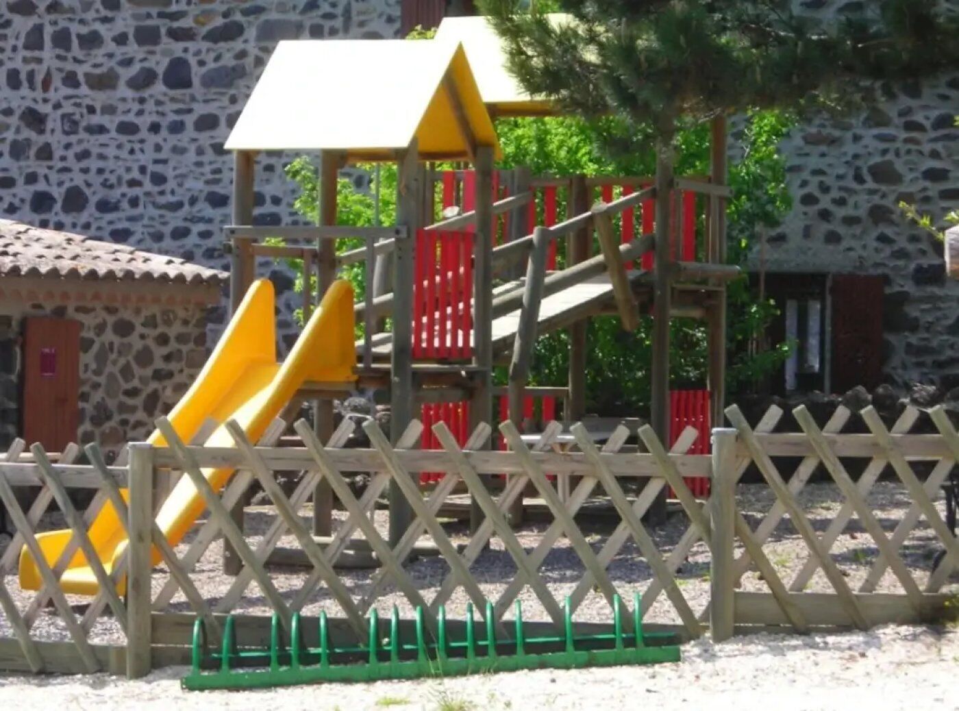 Un parque infantil con un tobogán amarillo y una estructura para escalar, rodeado por una valla de madera.