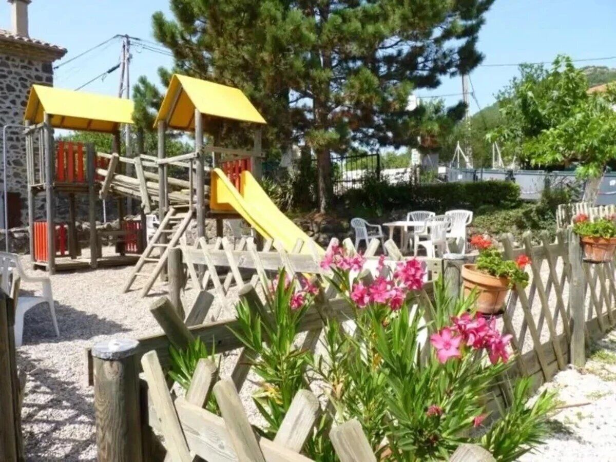 A playground with a slide and climbing structures, surrounded by a wooden fence and potted plants.