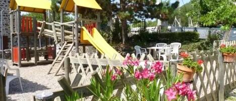 A playground with a slide and climbing structures, surrounded by a wooden fence and potted plants.