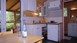 A compact kitchen with white cabinets, a small refrigerator, and a window providing natural light. - ZEcamping 3 étoiles pataugeoire pet friendly animations chalet 22m2 5 pers (Darbres)