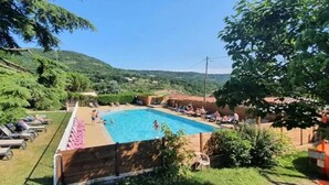 A swimming pool surrounded by lounge chairs and greenery, with a view of hills in the background. - ZEcamping 3 étoiles pataugeoire pet friendly animations chalet 22m2 5 pers (Darbres)