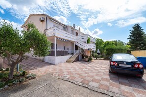 A two-story house with a checkered driveway, a car parked in front, and a satellite dish on the roof. - Apartments Valy 5 Center Novalja (Novalja)