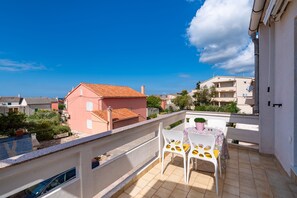 Een balkon met een tafel en stoelen, een uitzicht op omliggende gebouwen en een heldere lucht.