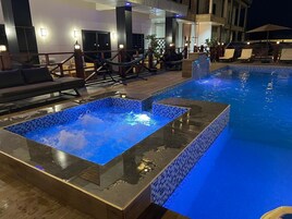 Una piscina con zona de hidromasaje de fondo de cristal, sillas de descanso y una terraza de madera.