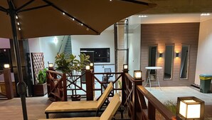 A covered outdoor seating area with cushioned chairs and tables, surrounded by wooden railings and potted plants. - Yasmin Luxury Resort (Paramaribo)