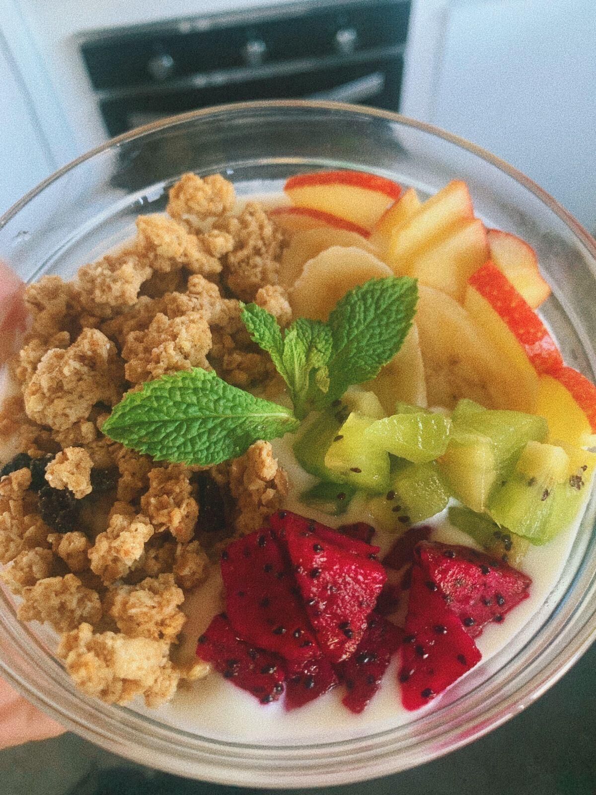 A bowl of cereal with fruits and a mint leaf.