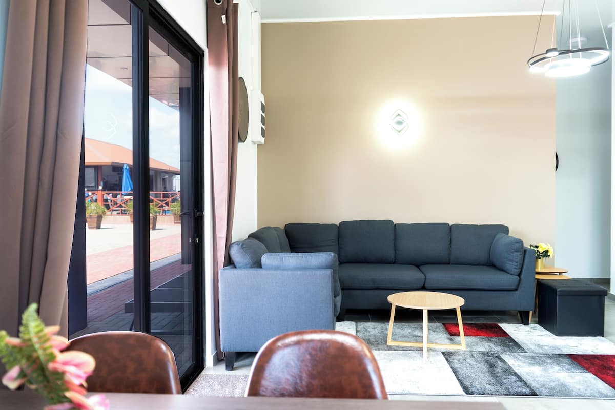 Ein modernes Wohnzimmer mit einem grauen Sofa, einem kleinen Holztisch und einem rot-grauen Teppich.