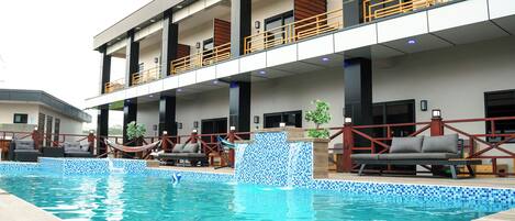 A modern hotel with a swimming pool, outdoor seating, and a covered terrace.
