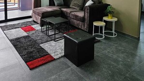 A modern living room with a sectional sofa, a coffee table, a side table, and a potted plant. There is a sliding glass door leading to an outdoor area. - Yasmin Luxury Resort (Paramaribo)