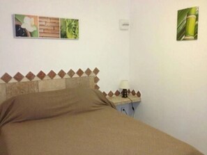 A bedroom with a bed, a nightstand with a lamp, and a wall with three framed pictures.
