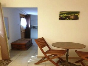 A room with a round table and two wooden chairs, a wooden chest, and a painting on the wall.