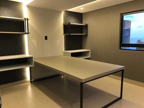 Una habitación moderna con una mesa grande, estanterías empotradas y un televisor fijado a la pared.