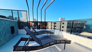 Une terrasse sur le toit, dotée de deux chaises longues et d’une balustrade en verre.