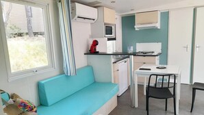 A compact kitchen with a microwave, stove, and sink. There's a teal sofa and a dining table with chairs.