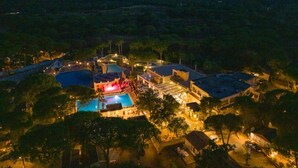 An aerial view of a resort with multiple swimming pools, a central building with a stage, and surrounding villas.