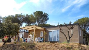 A single-story mobile home with a covered patio area, a small deck, and a window overlooking a grassy area.