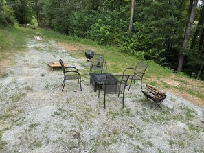 An outdoor seating area with metal chairs and a table, surrounded by gravel and greenery. - New Cozy Secluded Cabin with wi-fi (Rogers)