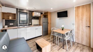 Une cuisine moderne avec des armoires blanches, une cuisinière encastrée et un réfrigérateur. On y trouve également un coin repas avec une table en bois et des chaises blanches.