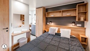 Une chambre moderne avec un grand lit, une tête de lit en bois, des étagères intégrées et une coiffeuse avec un miroir.