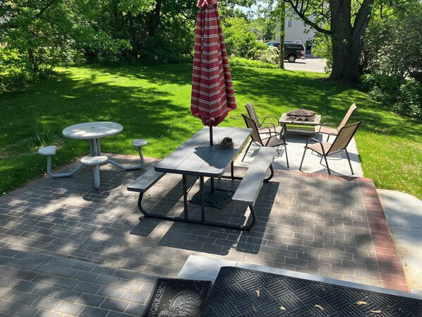 Un patio con una mesa y sillas, una mesita redonda y un paraguas rojo.