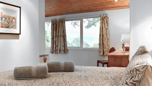 Un dormitorio con una colcha estampada, techo de madera, un escritorio con lámpara y una ventana con cortinas.
