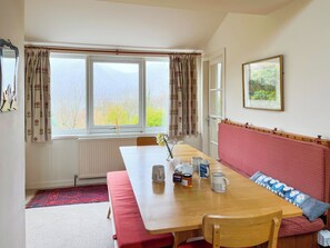 A dining area with a wooden table, chairs, a bench, a radiator, a window with curtains, and a framed picture on the wall.