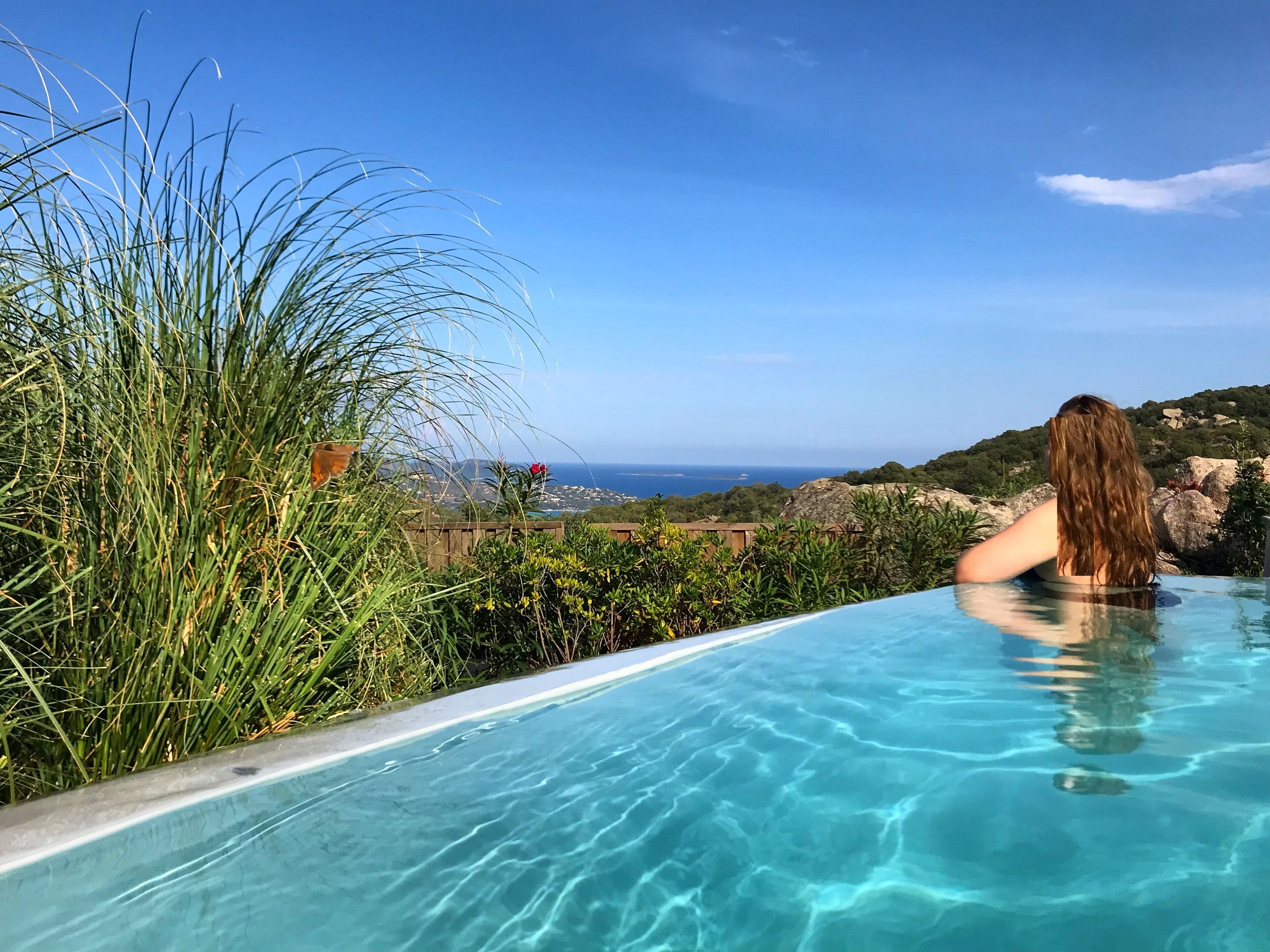 Ein Pool mit klarem Wasser, umgeben von viel Grün und mit Blick auf eine schöne Landschaft aus Meer und Hügeln.