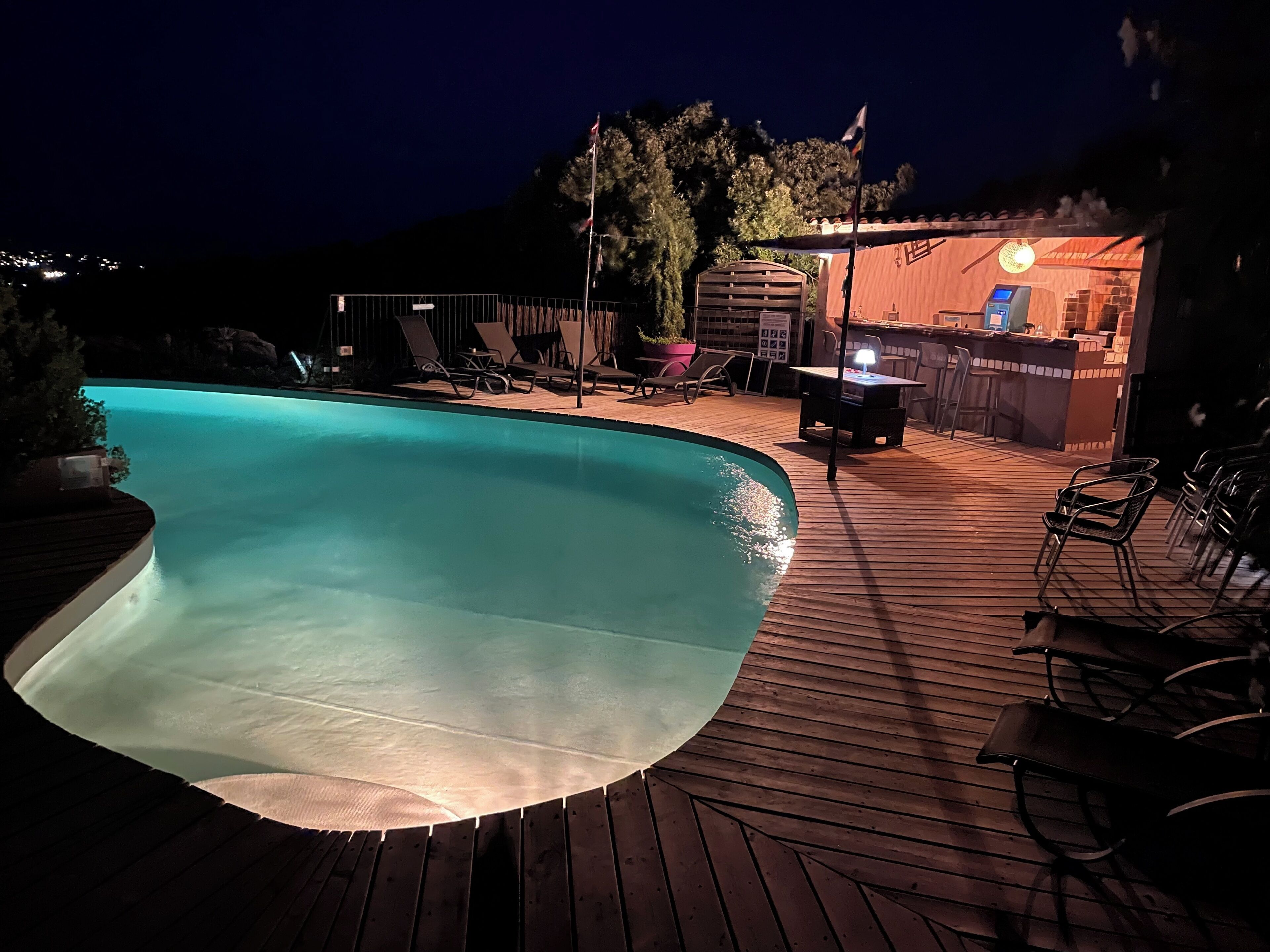 Une piscine dotée d’une terrasse en bois, de chaises longues et d’un espace bar avec un luminaire.