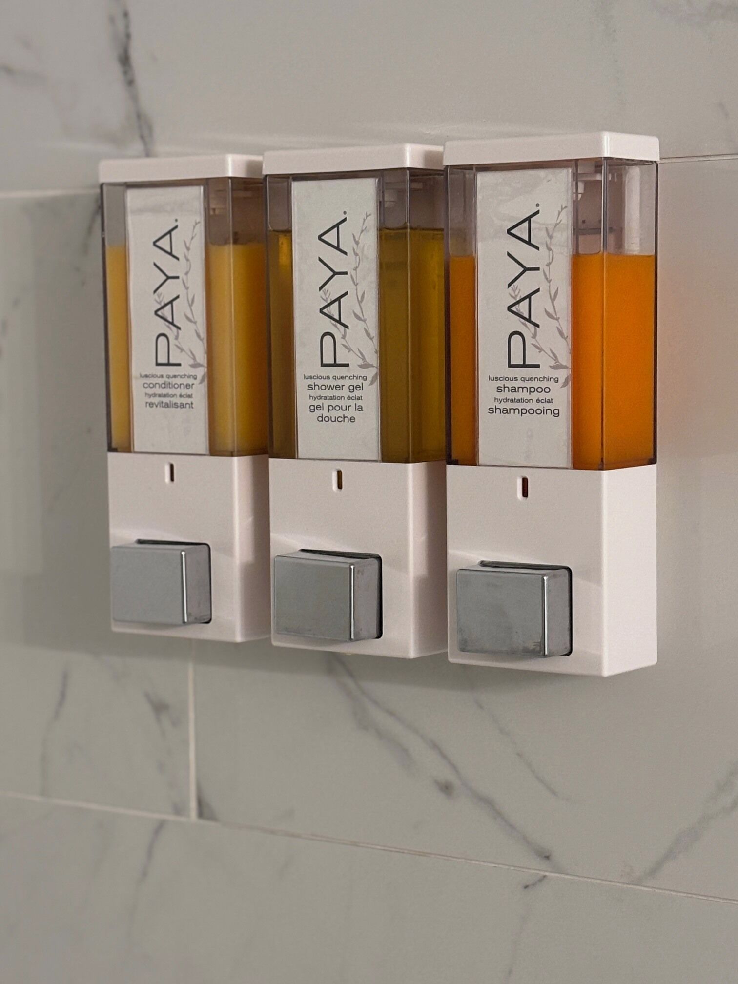 Un dispenser a parete con tre flaconi di gel doccia, balsamo e shampoo Paya.