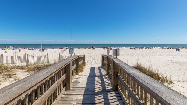 A wooden boardwalk leading to a sandy beach with clear skies.