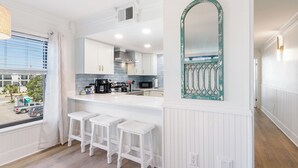 A modern kitchen with white cabinetry, a large island with bar stools, a vintage mirror, and a view of the street through a window.