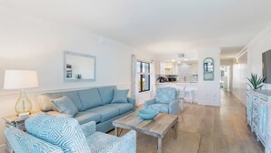 A modern living room with a sofa, patterned chairs, a coffee table, and a kitchen in the background.