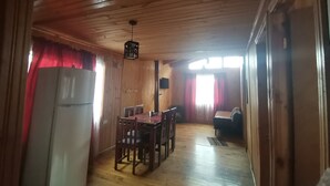 A wooden interior with a dining table and chairs, a sofa, a refrigerator, and a ceiling light fixture. - Cabañas EcoSur-Chile  (Curacautin)