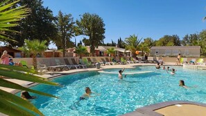 Una piscina con varias personas nadando, rodeada de sillas de descanso y palmeras.