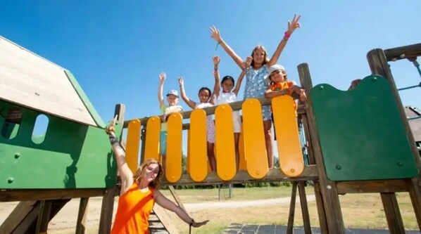 Un grupo de niños en una estructura de juego de madera con detalles amarillos.