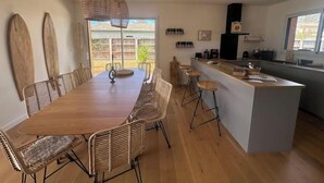 Eine moderne Küche mit einer zentralen Kochinsel, Barhocker und einem Essbereich mit einem langen Holztisch und Korbstühlen.