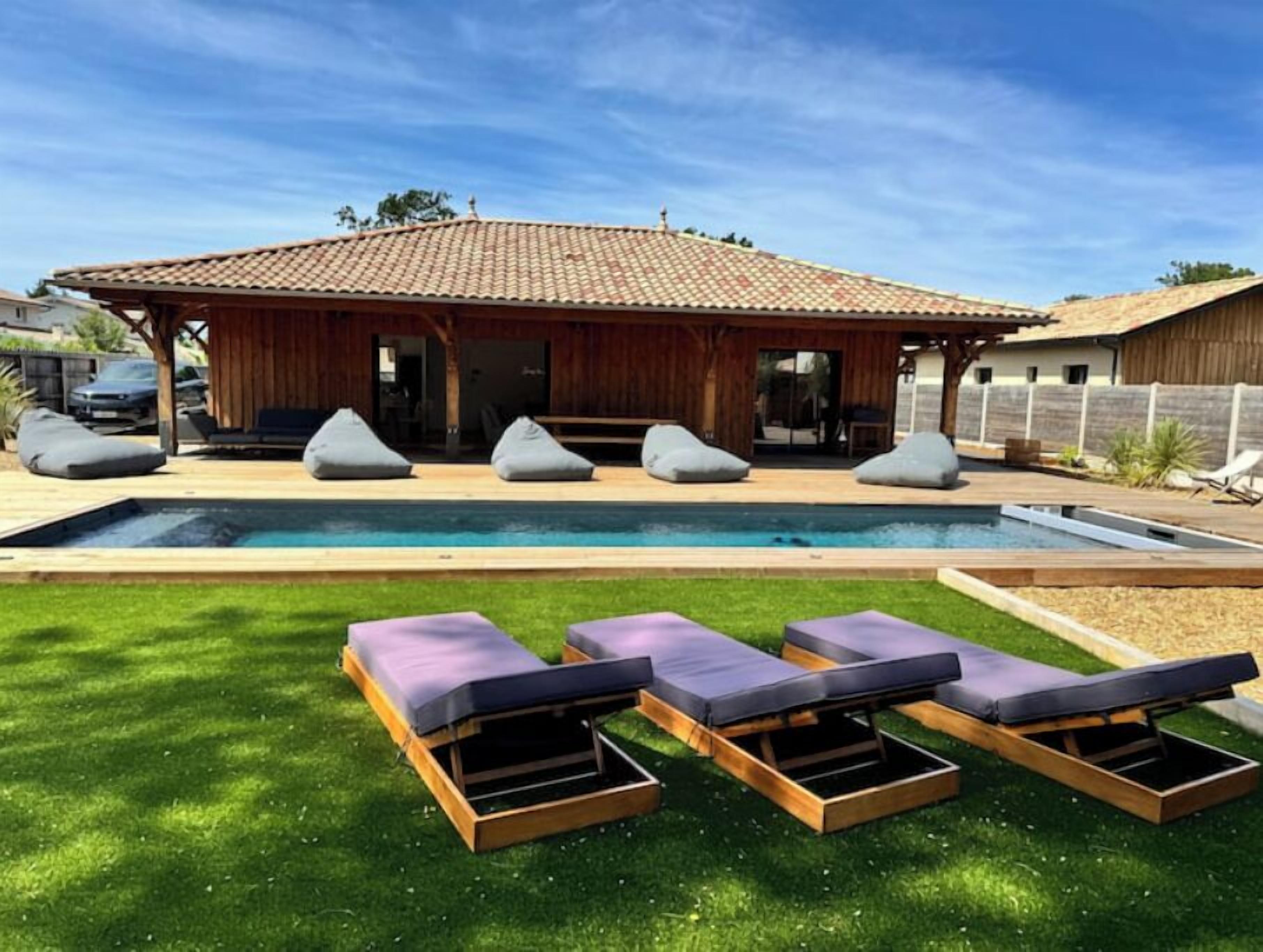 A poolside area with a wooden deck, a pool, and three lounge chairs.