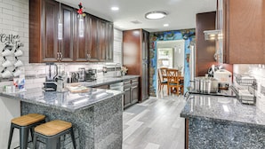 A kitchen with granite countertops, wooden cabinets, and a central island with stools. - ~ 2 Blocks to Beach: Galveston Group Getaway! (Galveston)