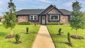 A two-story house with a brick facade, a front porch, and a well-maintained lawn with young trees. - ~ 2 Blocks to Beach: Galveston Group Getaway! (Galveston)