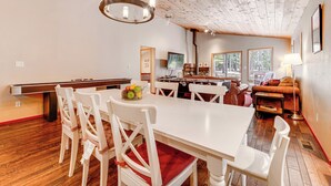 A spacious dining area with a long white table and chairs, a wooden ceiling, and a view of the outdoors through large windows. - Home w/ Deck + Access to Tahoe Donner Amenities! (Truckee)