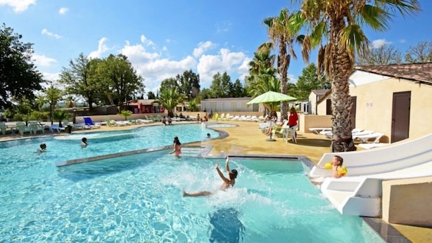 Una piscina con sillones de descanso y palmeras.