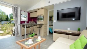 Una sala de estar moderna con un sofá, un televisor montado en la pared y una zona de cocina con taburetes de bar.