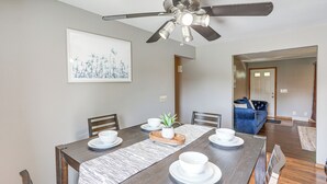 Un coin repas avec une table en bois dressée pour quatre personnes, un ventilateur de plafond et une œuvre d’art encadrée accrochée au mur.