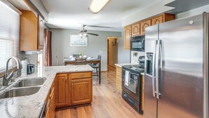Une cuisine moderne avec des meubles en bois, des appareils en acier inoxydable, un plan de travail en granit et un ventilateur de plafond.
